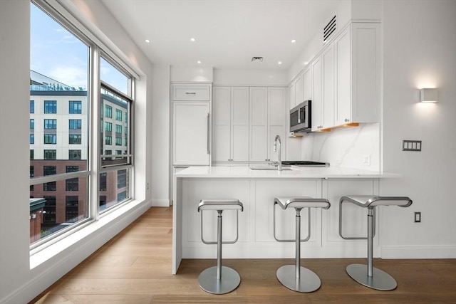 700 Harrison Ave Unit Ph-610, Boston, MA 02118 - kitchen featuring a peninsula, a sink, stainless steel microwave, light wood finished floors, and white cabinetry
