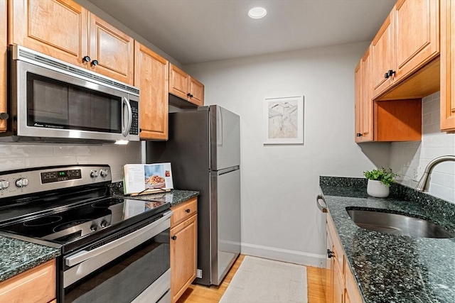 kitchen featuring stainless steel appliances, a sink, decorative backsplash, baseboards, and dark stone countertops