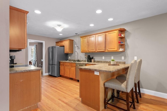 kitchen with appliances with stainless steel finishes, sink, hanging light fixtures, kitchen peninsula, and light hardwood / wood-style flooring