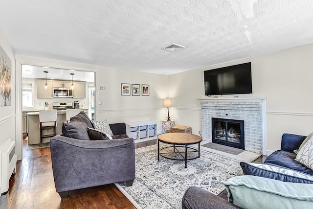 living area with a textured ceiling, a fireplace, wood finished floors, visible vents, and radiator