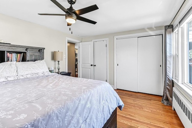 bedroom featuring multiple closets, light wood-type flooring, radiator, and a ceiling fan