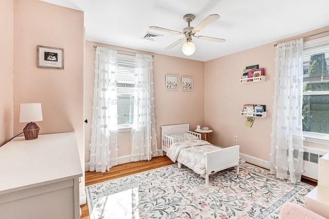 bedroom with radiator, visible vents, a ceiling fan, wood finished floors, and baseboards