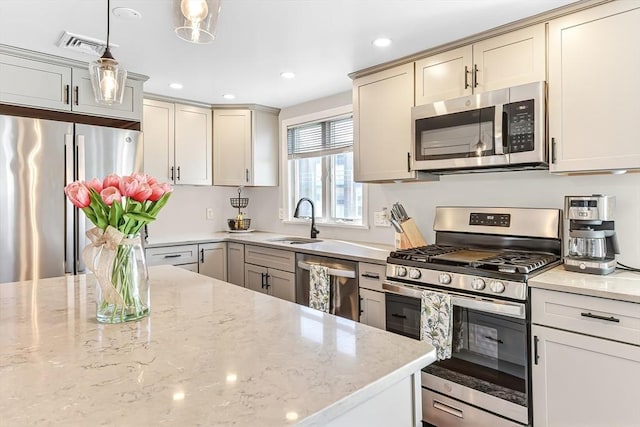 kitchen with recessed lighting, a sink, appliances with stainless steel finishes, light stone countertops, and pendant lighting