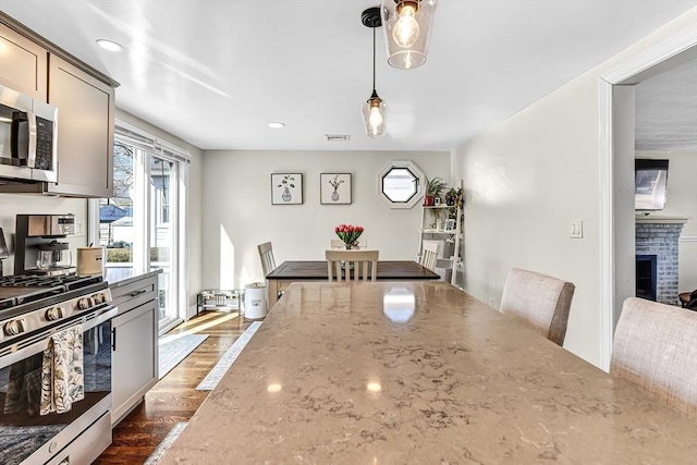 kitchen with light stone counters, stainless steel appliances, a fireplace, visible vents, and dark wood-style floors