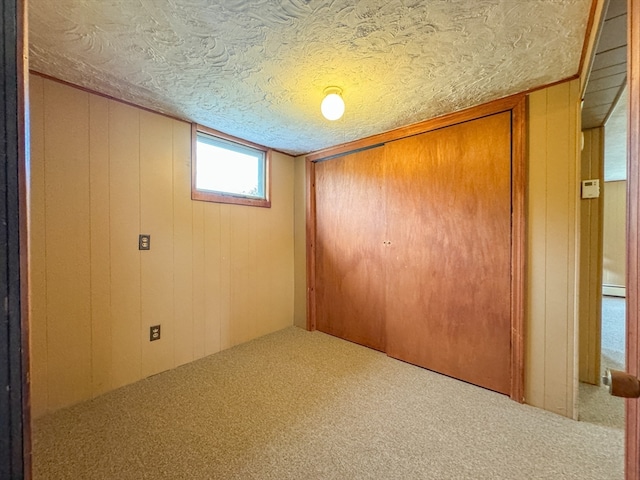 unfurnished bedroom featuring carpet, wood walls, a closet, and a textured ceiling