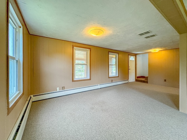 carpeted spare room featuring a baseboard radiator, wooden walls, and a textured ceiling