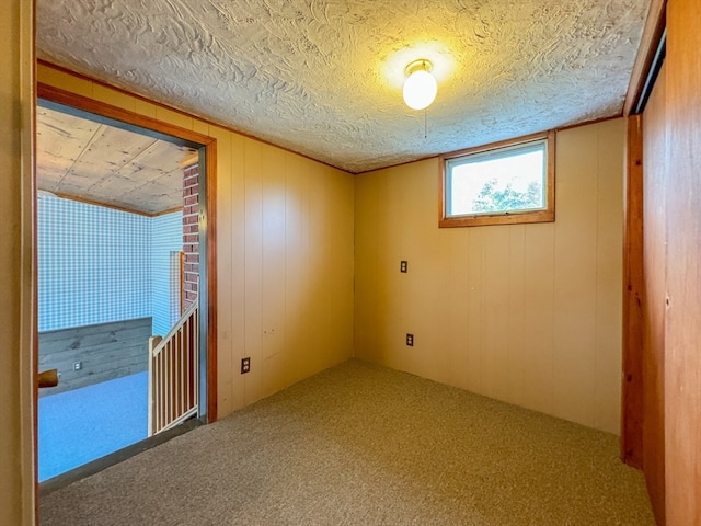 unfurnished room featuring a textured ceiling, wooden walls, and carpet flooring