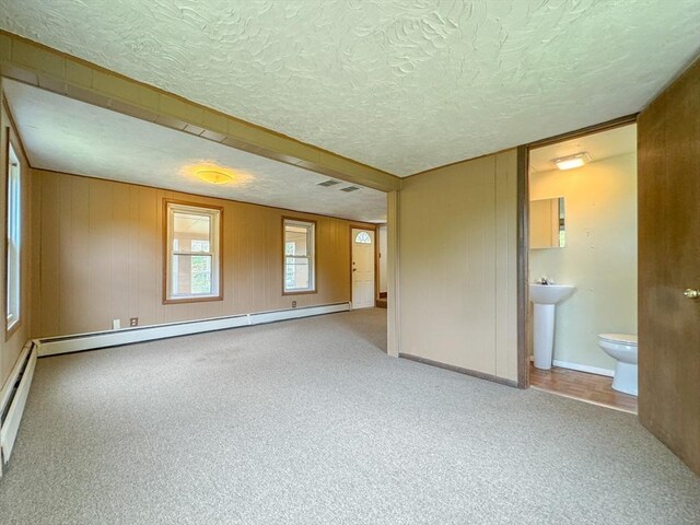 carpeted empty room with a textured ceiling, baseboard heating, and sink