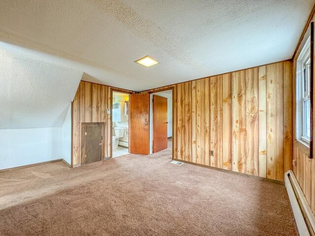 additional living space featuring a textured ceiling, baseboard heating, and wood walls