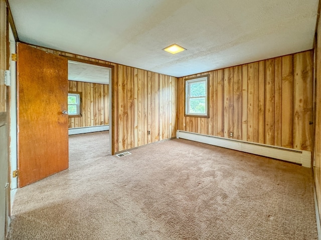 carpeted spare room with wooden walls, a textured ceiling, and baseboard heating