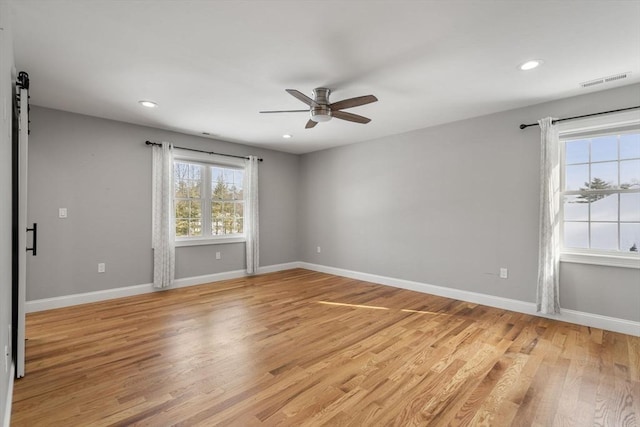 spare room with ceiling fan, a barn door, and light wood-type flooring