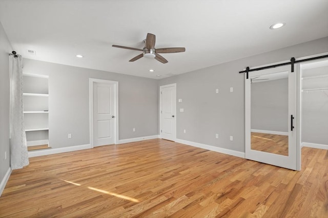 unfurnished bedroom featuring a walk in closet, ceiling fan, a barn door, and light hardwood / wood-style floors