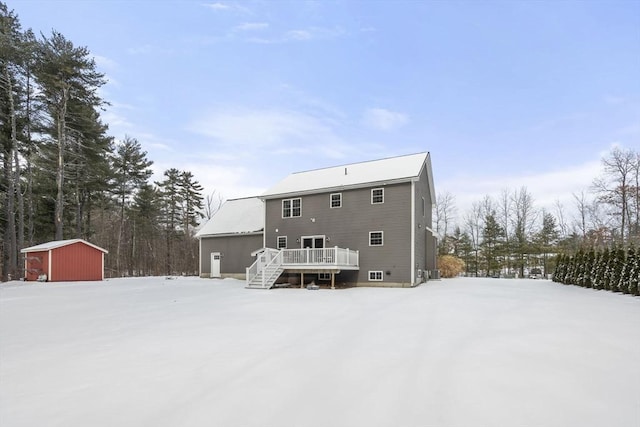 snow covered back of property featuring a wooden deck and a storage unit