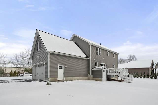 snow covered back of property with a garage and a deck