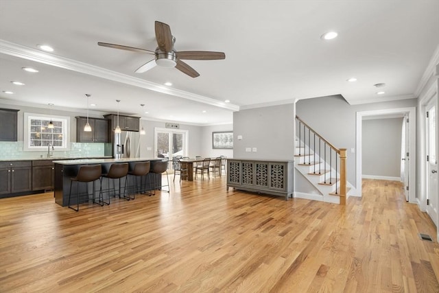 living room featuring ceiling fan, ornamental molding, light hardwood / wood-style floors, and sink