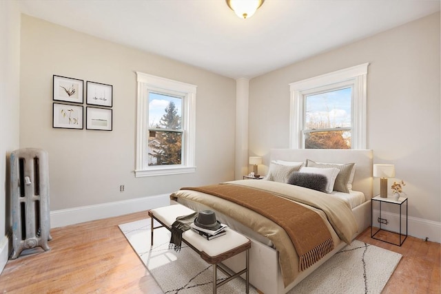 bedroom with light hardwood / wood-style floors, radiator heating unit, and multiple windows