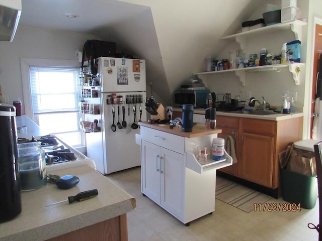 kitchen featuring white refrigerator, lofted ceiling, white cabinets, and sink