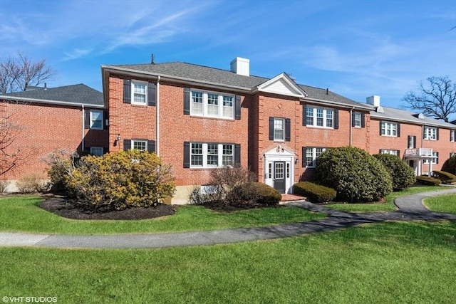 view of front of house with a front yard, brick siding, and a chimney