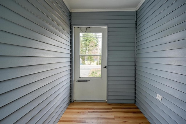 doorway to outside with light wood-style floors, crown molding, and wooden walls