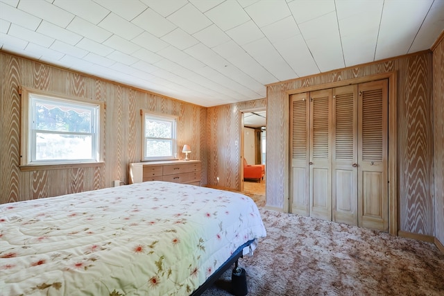 carpeted bedroom with wooden walls and a closet