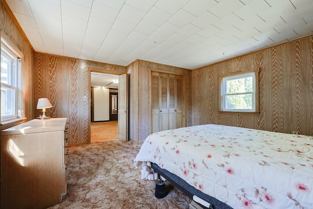 carpeted bedroom with wood walls, a closet, and multiple windows