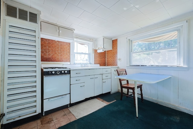 kitchen featuring dark tile patterned flooring, a healthy amount of sunlight, white range oven, and white cabinetry