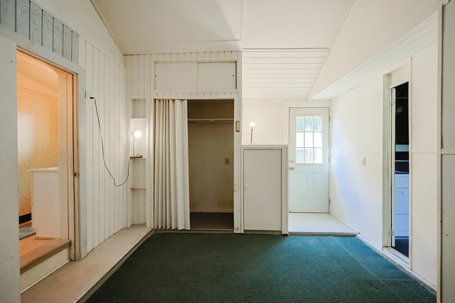 corridor with wooden walls, dark carpet, and lofted ceiling