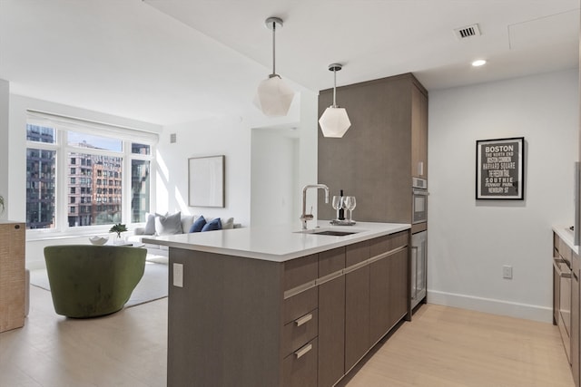 kitchen with oven, sink, kitchen peninsula, light hardwood / wood-style floors, and pendant lighting