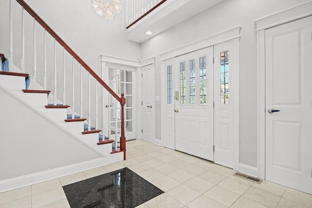 tiled foyer featuring a high ceiling, stairway, baseboards, and visible vents