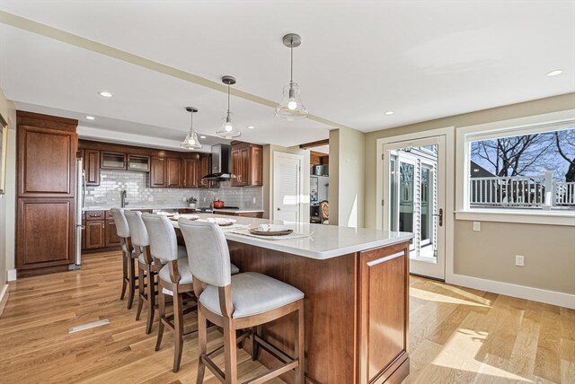 17 Wagon Wheel Rd, Winchester, MA 01890 - kitchen featuring wall chimney range hood, light countertops, baseboards, light wood-style floors, and decorative backsplash