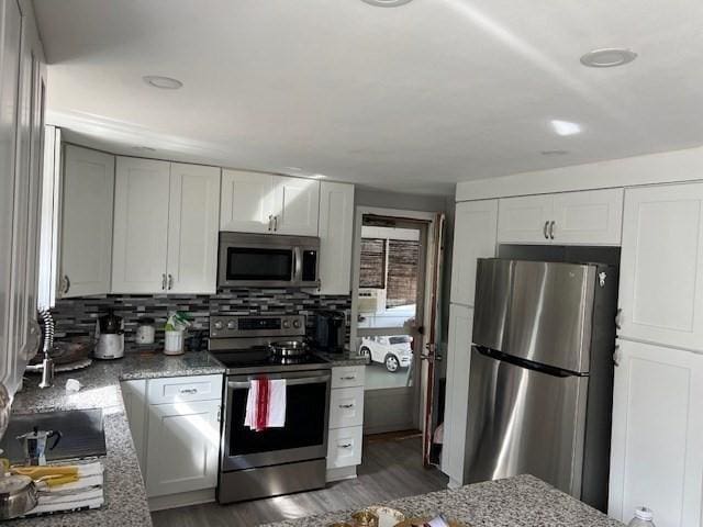 kitchen featuring backsplash, wood finished floors, appliances with stainless steel finishes, white cabinets, and light stone countertops