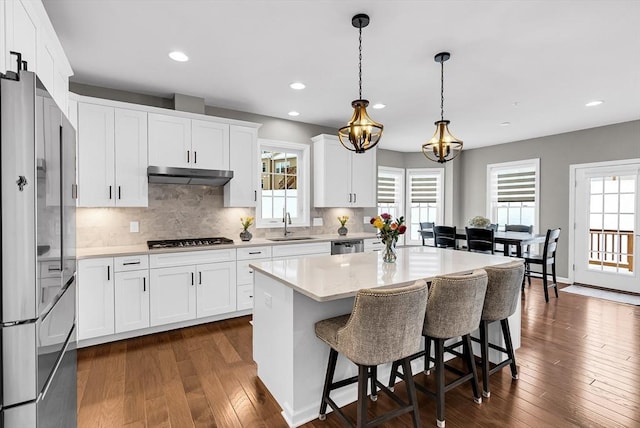 kitchen with decorative light fixtures, white cabinetry, stainless steel appliances, and a kitchen island