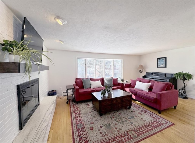 living room with a brick fireplace, a textured ceiling, light hardwood / wood-style floors, and baseboard heating