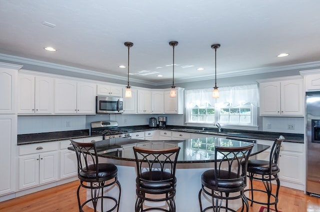 kitchen with white cabinets, appliances with stainless steel finishes, a kitchen island, and light hardwood / wood-style floors