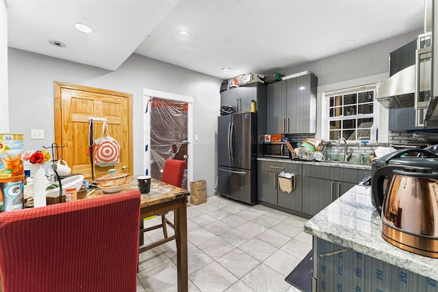 kitchen featuring backsplash, sink, stainless steel fridge, light stone countertops, and range hood