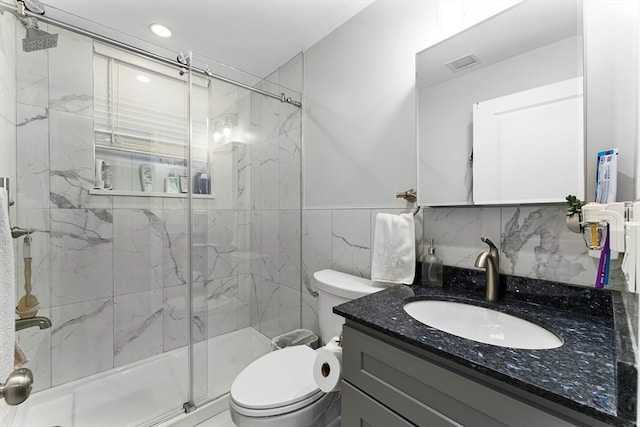 bathroom with vanity, toilet, a shower with shower door, and tile walls