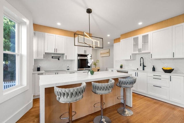 kitchen with light wood finished floors, a sink, oven, white cabinets, and black electric cooktop