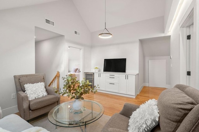 living area with light wood-type flooring, visible vents, wine cooler, and high vaulted ceiling