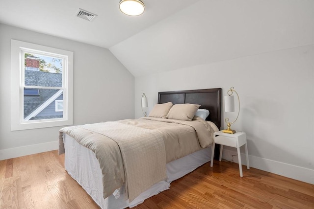 bedroom with visible vents, baseboards, light wood-type flooring, and lofted ceiling