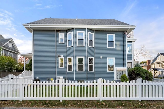 view of side of home featuring a fenced front yard and a shingled roof