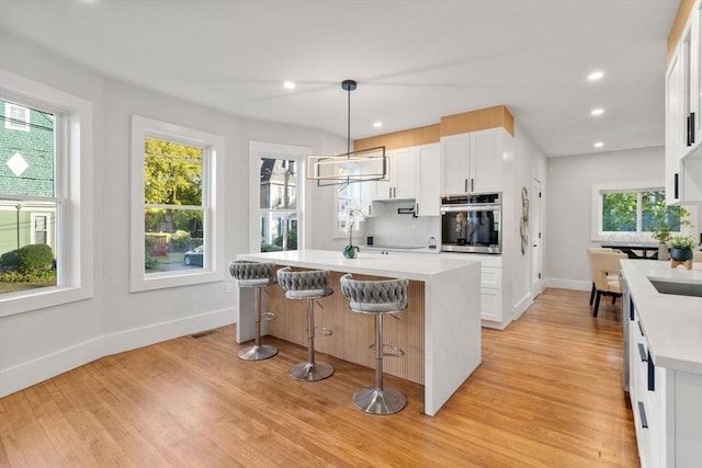 kitchen featuring decorative backsplash, white cabinets, light countertops, and stainless steel oven