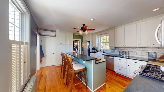 kitchen featuring a wall unit AC, light hardwood / wood-style flooring, stainless steel appliances, a kitchen bar, and white cabinets