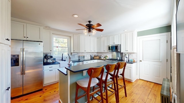 kitchen with a kitchen bar, appliances with stainless steel finishes, light hardwood / wood-style flooring, and white cabinets