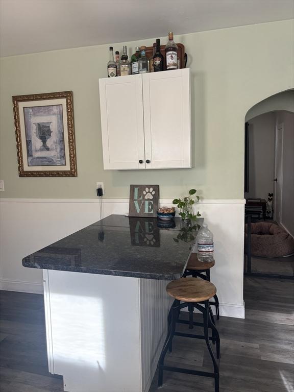 bar with dark stone countertops, dark hardwood / wood-style floors, and white cabinets