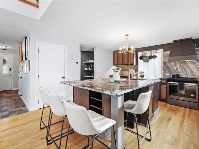 kitchen with a center island, stainless steel range with electric cooktop, hanging light fixtures, wall chimney exhaust hood, and light stone countertops