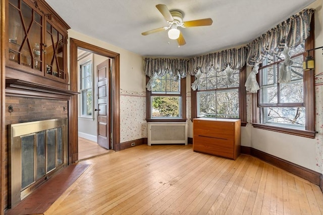 unfurnished dining area with light wood finished floors, baseboards, radiator heating unit, a brick fireplace, and ceiling fan