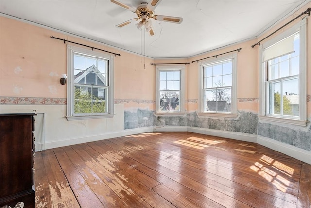 spare room featuring wainscoting, wood-type flooring, a ceiling fan, and a healthy amount of sunlight