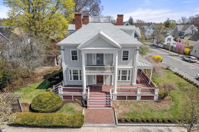 neoclassical home featuring a chimney, covered porch, and a balcony