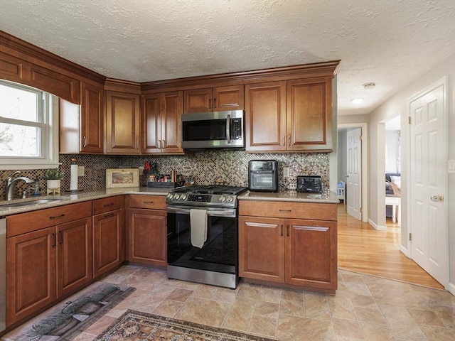 kitchen with appliances with stainless steel finishes, a sink, tasteful backsplash, a textured ceiling, and light countertops