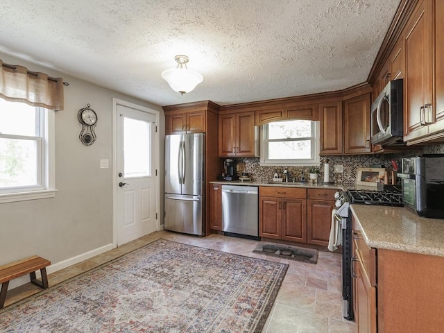 kitchen with stainless steel appliances, a sink, healthy amount of natural light, brown cabinets, and a textured ceiling